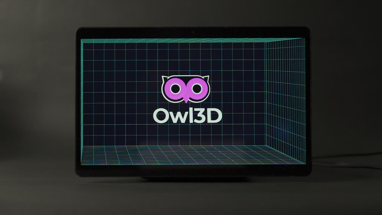 The Owl3D Shift seen from the front on a dark surface, its screen showing the Owl3D logo inside a grid-lined room.