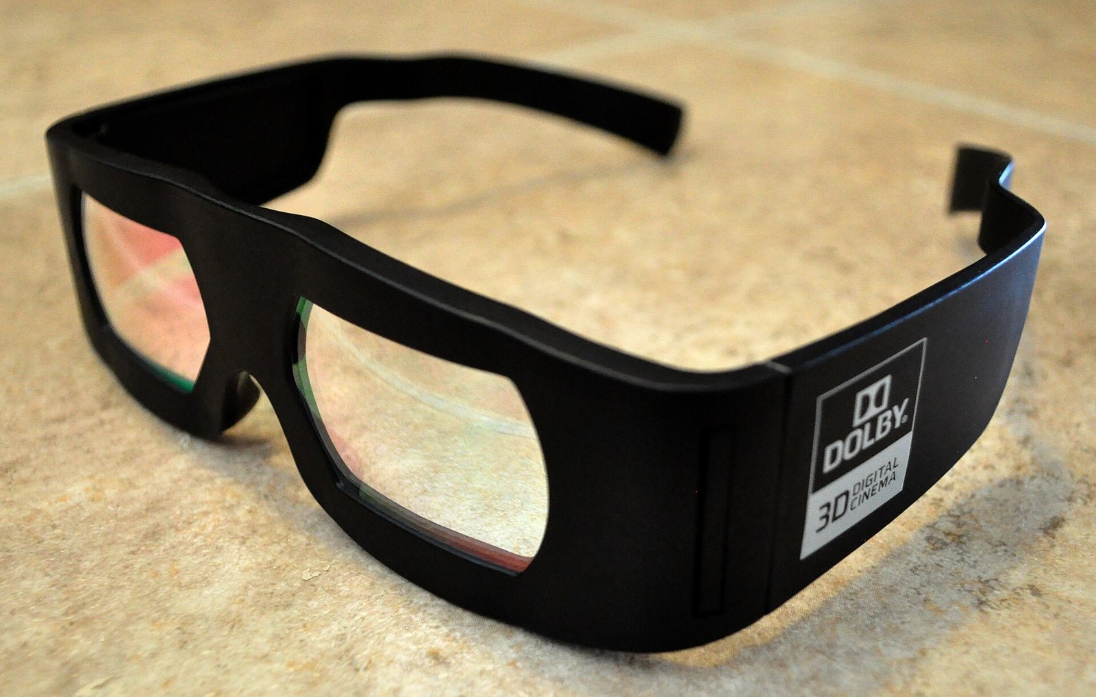 A pair of black plastic Dolby 3D cinema glasses whose lenses reflect pink and green, with a Dolby 3D Digital Cinema label on the temple.