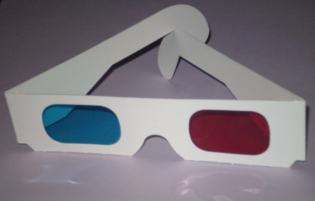 A pair of white paper 3D glasses standing on a table, with one cyan filter and one red filter.