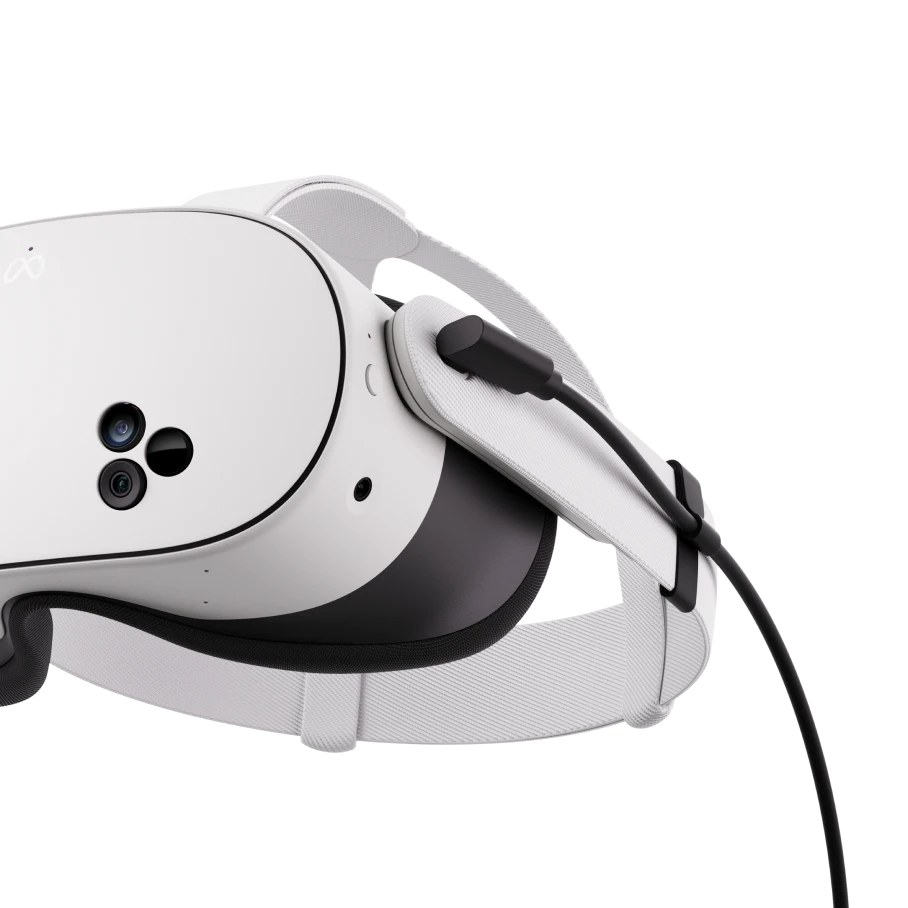 A white Meta Quest headset seen from the side, with a black USB-C cable plugged into it and clipped to the strap.