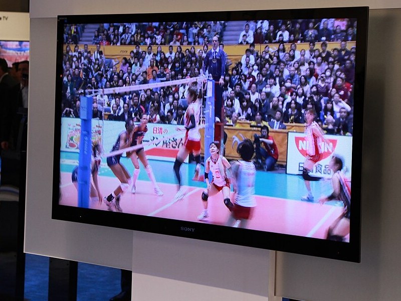 展示会場の白い壁に掛けられたソニーの薄型テレビ。画面にはバレーボールの試合が映っている。
