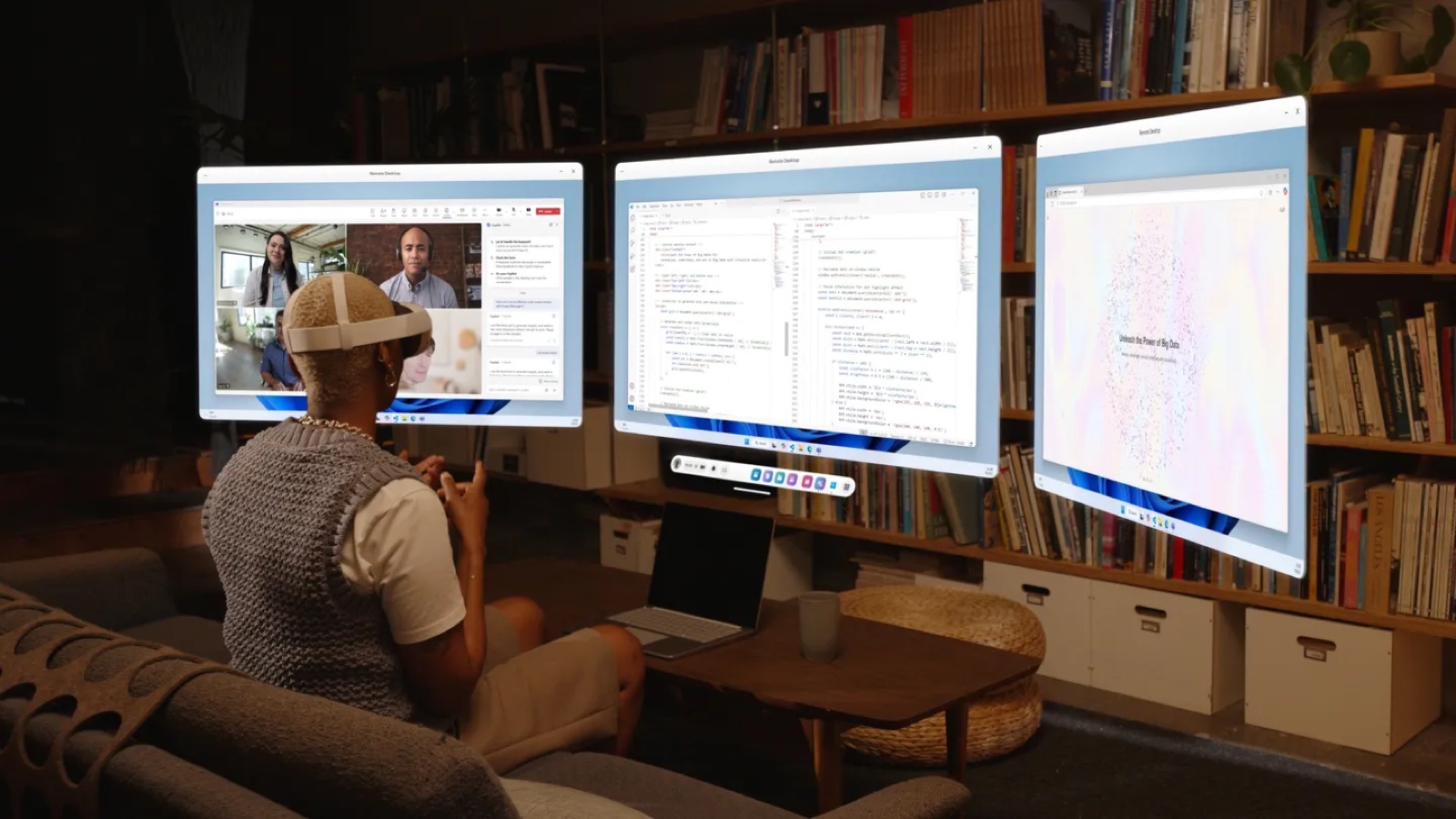 A person in a white VR headset sits on a sofa facing three large floating Windows 11 screens, with a laptop on the low table in front.
