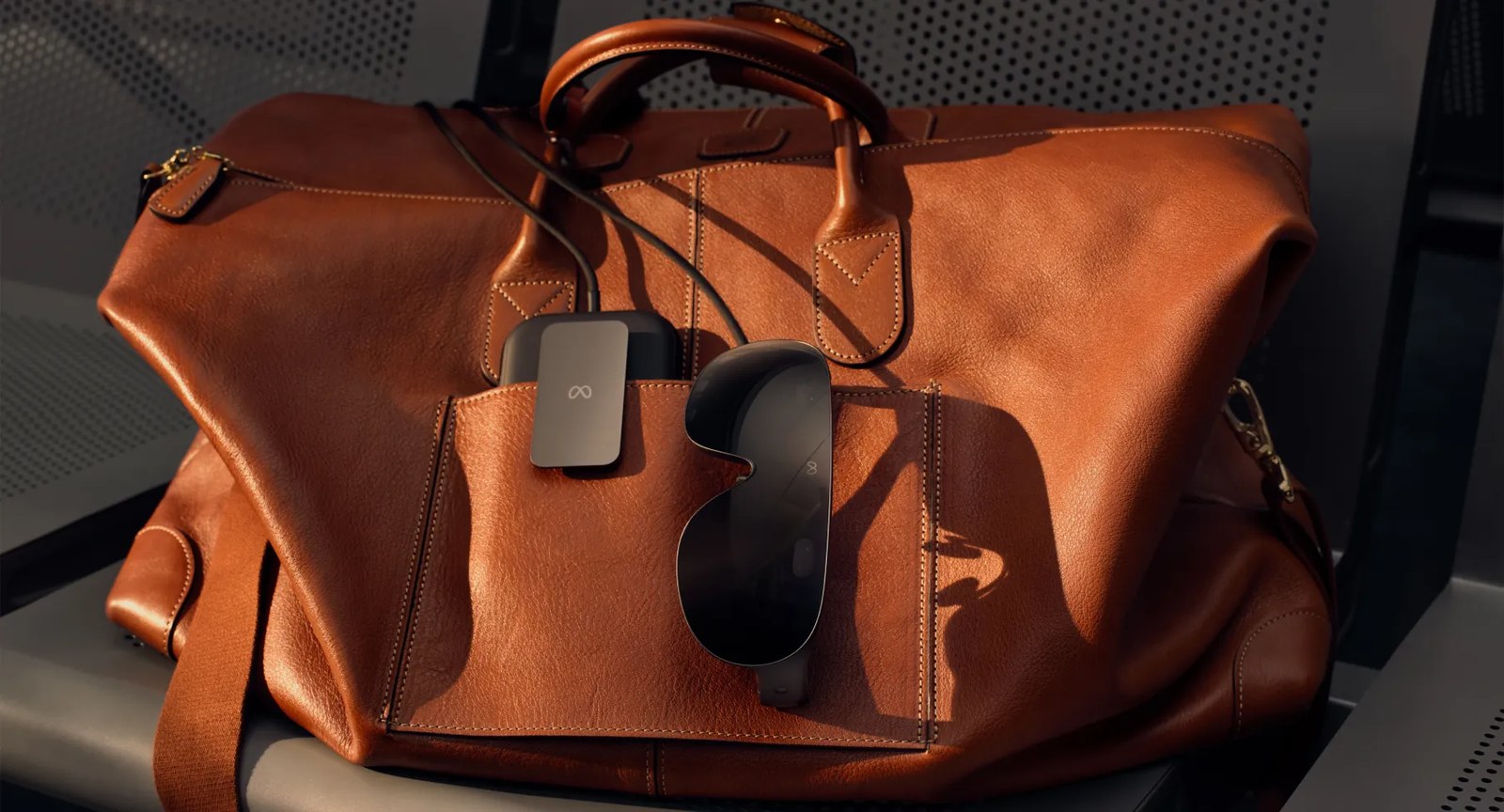 Meta VR Glasses and their puck tucked into the outer pocket of a brown leather bag, joined by a cable.