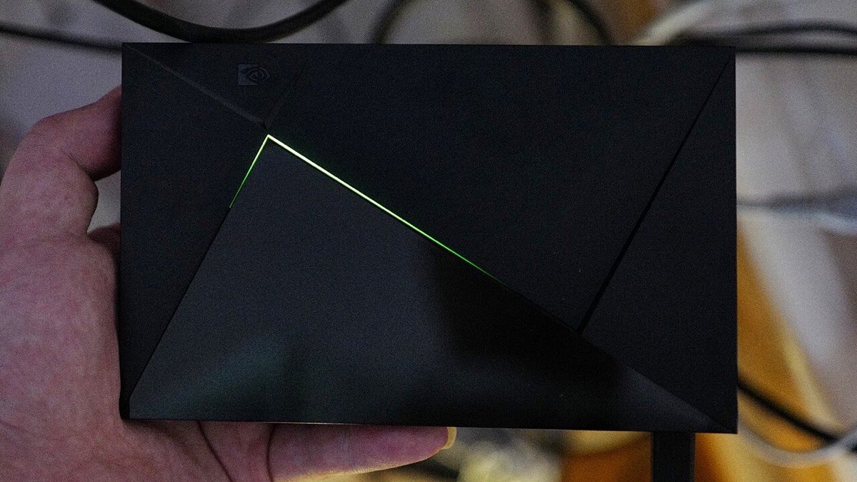 Eine schwarze NVIDIA-SHIELD-TV-Box in einer Hand, ihr grünes Licht leuchtet.