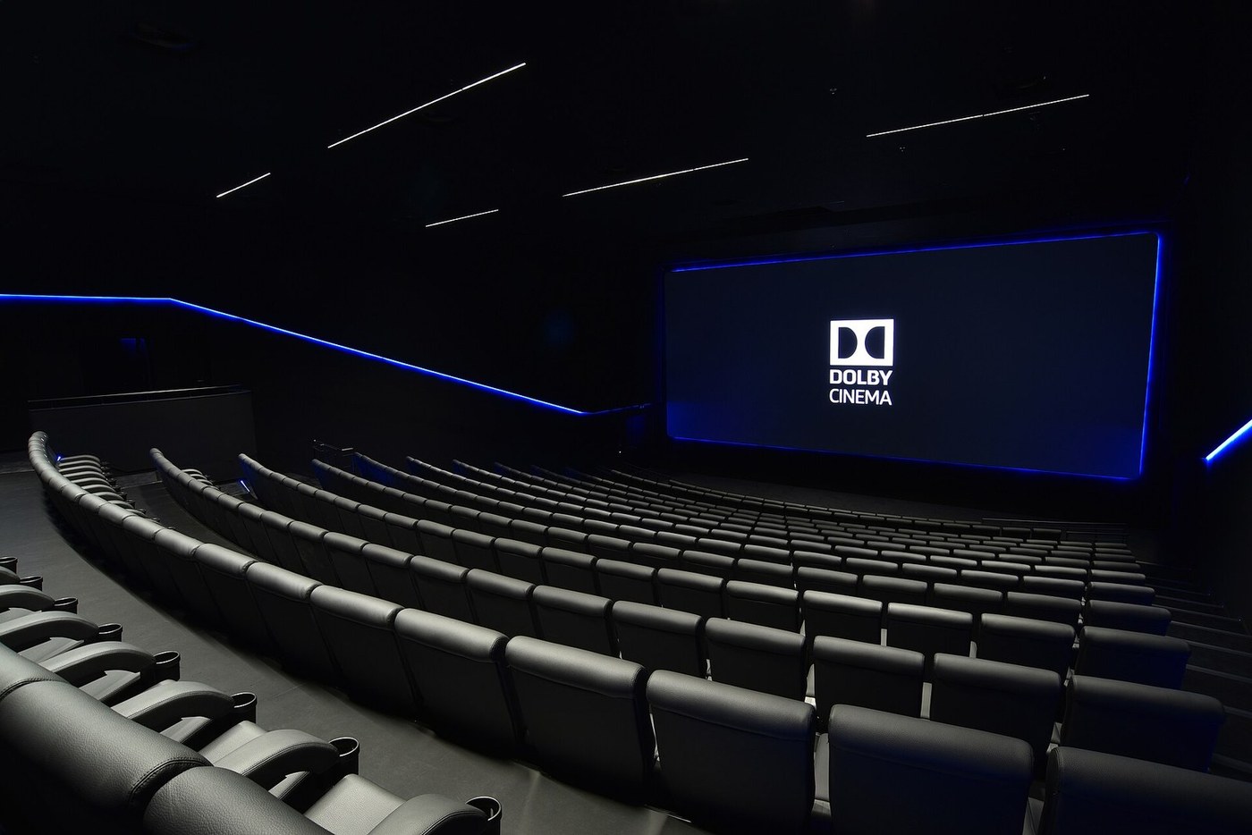 A dark Dolby Cinema auditorium with curved rows of black seats and the Dolby Cinema logo on the screen.