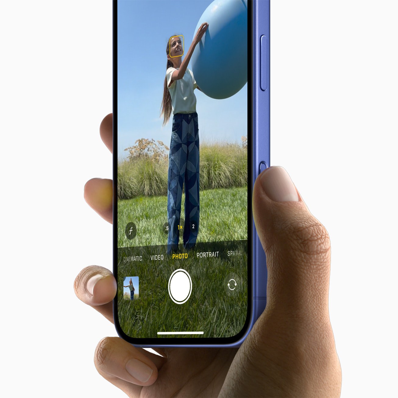 A hand holding an iPhone 16 with the Camera app open; the row of modes above the shutter button reads Cinematic, Video, Photo, Portrait, and Spatial at the right-hand edge.