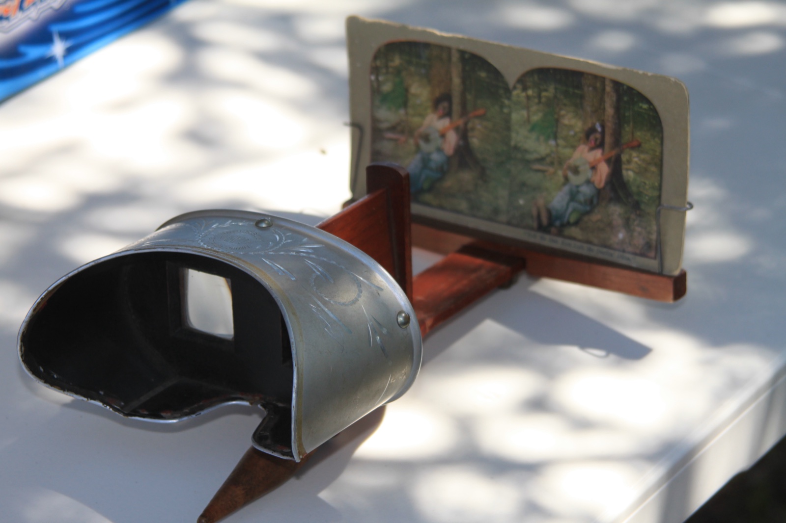 A hand-held stereoscope on a table, with a card in its holder that carries two nearly identical colour photographs side by side.