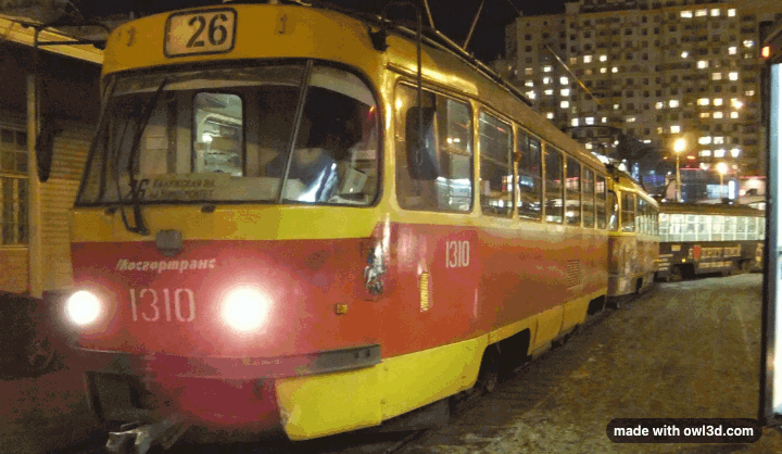 A night-time photo of a red and yellow tram that rocks back and forth between two viewpoints, so the tram stands out from the buildings behind it.