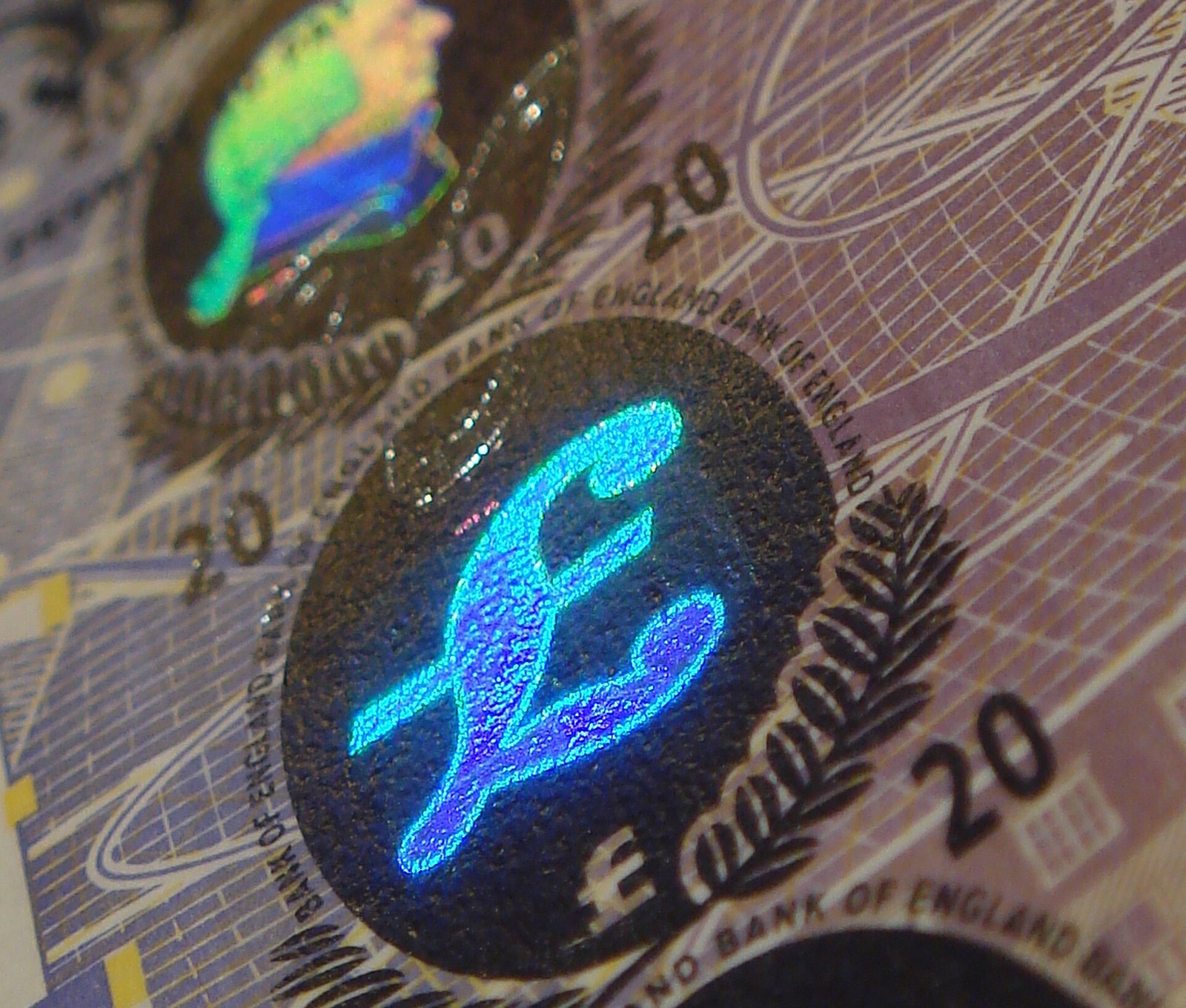 Close-up of the foil on a Bank of England 20 pound note, with a pound sign and other small images glowing in blue and green inside dark ovals.