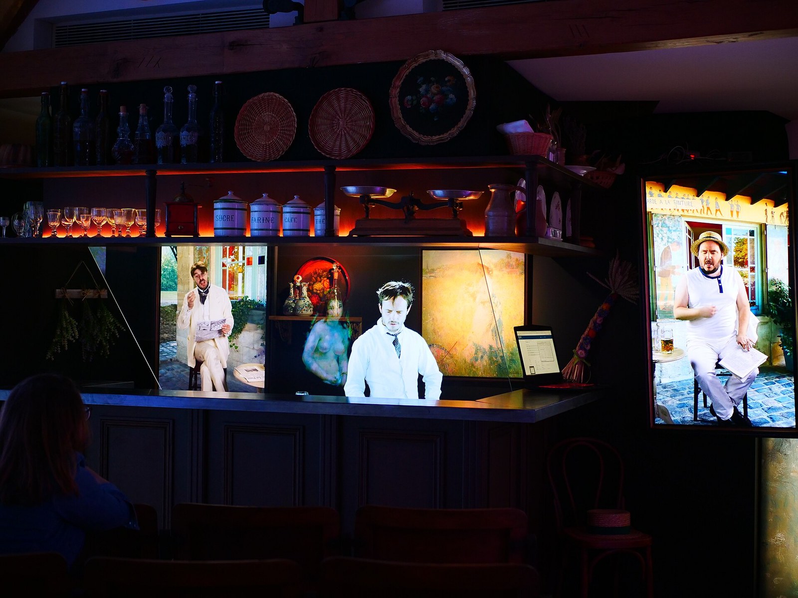 A dark room set up as a bar, with a pale, slightly see-through figure of a man in a white shirt standing behind the counter.