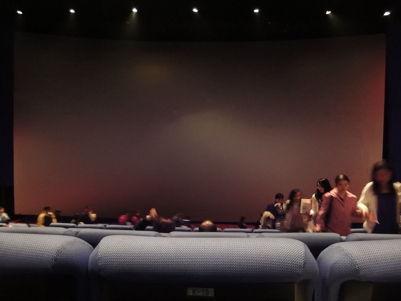 從觀眾席後排往前看的 IMAX 影廳,一塊巨大的銀幕佔滿前方整面牆,前排有觀眾正在走動、入座。